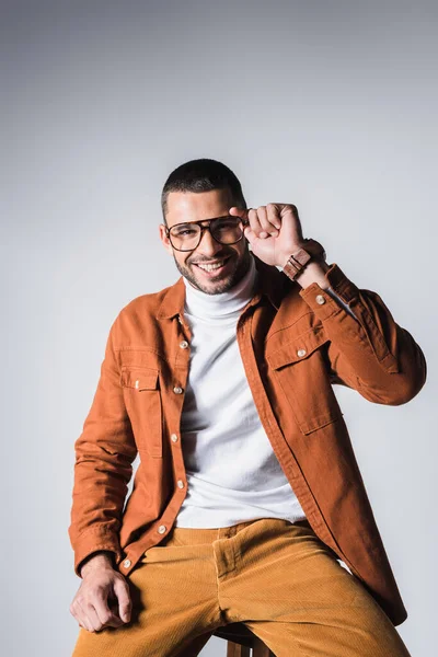 Hombre positivo sosteniendo anteojos mientras mira a la cámara sobre fondo gris - foto de stock