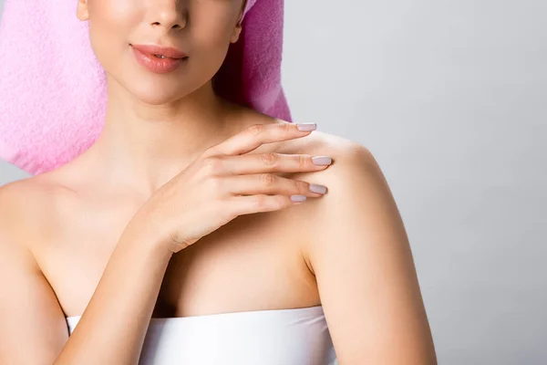 Cropped view of beautiful woman with towel on hair touching skin isolated on grey — Stock Photo