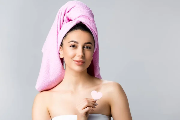 Hermosa mujer con toalla en el pelo celebración de corazón en forma de esponja aislada en gris - foto de stock