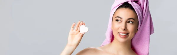Happy beautiful woman with towel on hair holding heart shaped sponge isolated on grey, banner — Stock Photo
