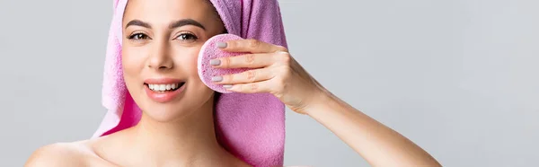 Smiling beautiful woman with towel on hair using sponge isolated on grey, banner — Stock Photo