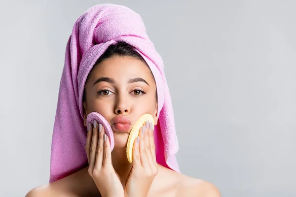 Красивая женщина с полотенцем на волосах с помощью губок на лице изолированы на сером — стоковое фото