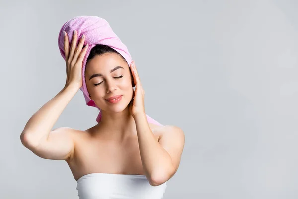 Mujer hermosa y complacida con toalla en el pelo aislado en gris - foto de stock