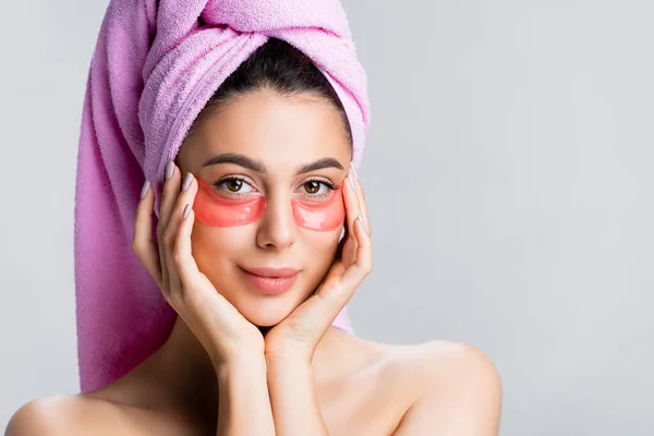 Bela mulher com toalha no cabelo e manchas olho hidrogel no rosto isolado em cinza — Fotografia de Stock