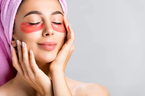 Beautiful woman with towel on hair and hydrogel eye patches on face isolated on grey — Stock Photo