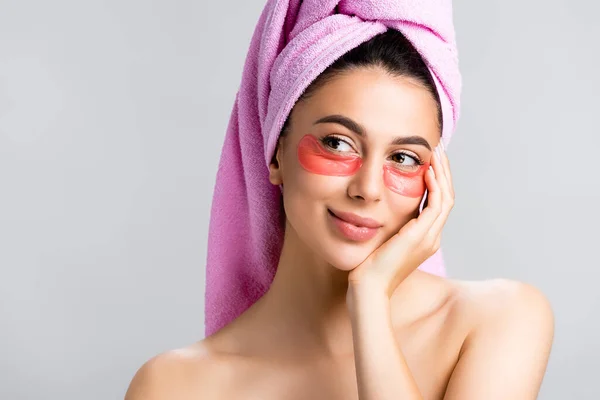 Dreamy beautiful woman with towel on hair and hydrogel eye patches on face isolated on grey — Stock Photo