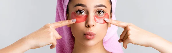 Bela mulher com toalha no cabelo apontando para manchas olho hidrogel no rosto isolado em cinza, banner — Fotografia de Stock