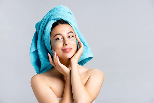 Lächelnd schöne Frau mit blauem Handtuch auf den Haaren und Hydrogel-Augenklappen auf dem Gesicht isoliert auf grau — Stockfoto