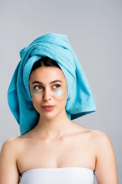 Belle femme avec serviette bleue sur les cheveux et cache-yeux hydrogel sur le visage isolé sur gris — Photo de stock