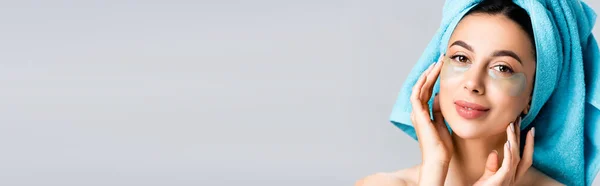 Smiling beautiful woman with blue towel on hair and hydrogel eye patches on face isolated on grey, banner — Stock Photo