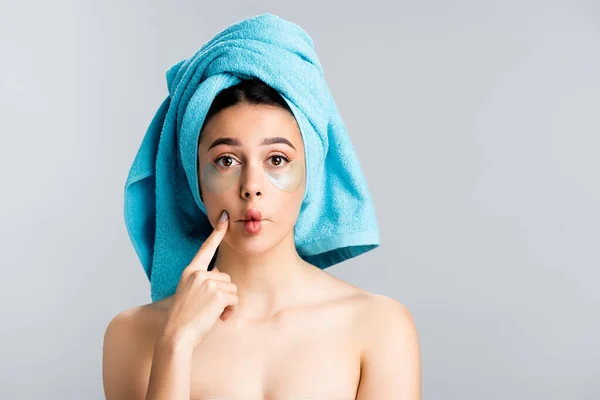 Bella donna con asciugamano blu sui capelli e macchie oculari idrogel sul viso sghignazzante isolato su grigio — Foto stock
