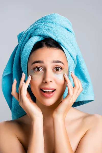 Amazed beautiful woman with blue towel on hair and hydrogel eye patches on face isolated on grey — Stock Photo