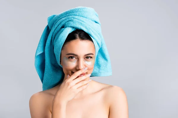 Hermosa mujer riendo con toalla azul en el cabello y parches de hidrogel en la cara aislado en gris - foto de stock