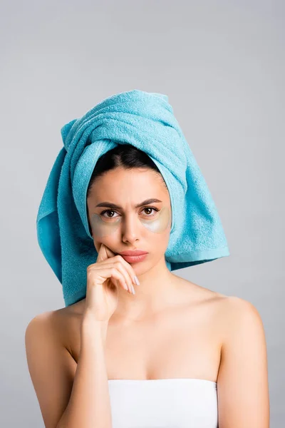 Mujer hermosa triste con toalla azul en el cabello y parches de hidrogel en la cara aislado en gris - foto de stock