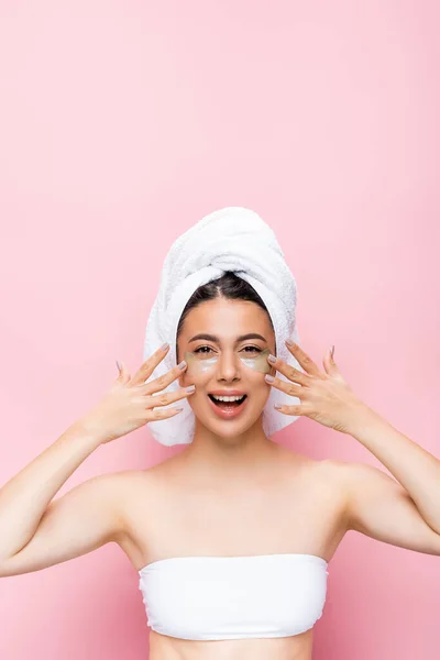 Glücklich schöne Frau mit Handtuch auf dem Haar und Hydrogel Augenflecken auf dem Gesicht isoliert auf rosa — Stockfoto