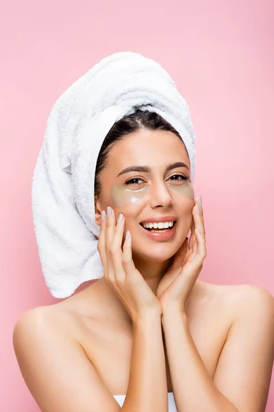 Mulher bonita sorridente com toalha no cabelo e manchas olho hidrogel no rosto isolado em rosa — Fotografia de Stock