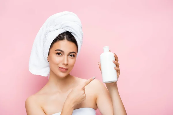 Beautiful woman with towel on hair pointing on bottle of lotion isolated on pink — Stock Photo