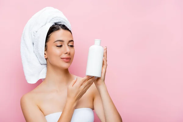 Belle femme avec serviette sur cheveux et bouteille de lotion isolée sur rose — Photo de stock