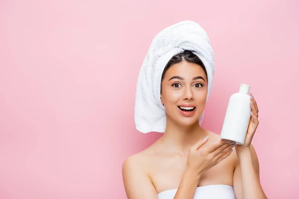 Happy beautiful woman with towel on hair and bottle of lotion isolated on pink — Stock Photo