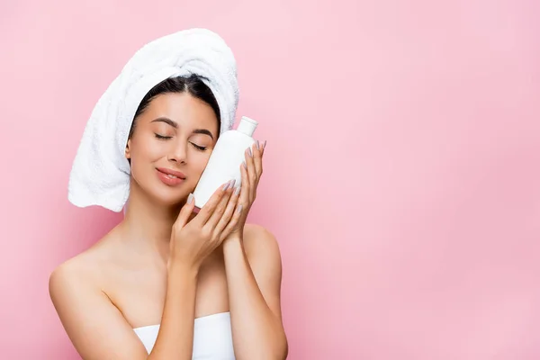 Beautiful woman with closed eyes, towel on hair and bottle of lotion isolated on pink — Stock Photo