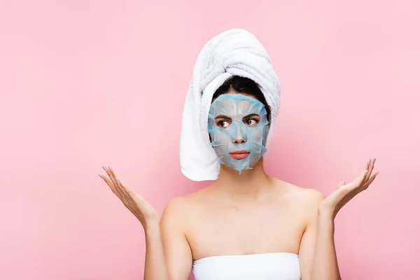 Belle femme avec feuille de masque sur le visage montrant haussement d'épaules isolé sur rose — Photo de stock