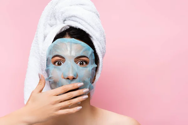 Impactado hermosa mujer con la hoja de máscara en la cara aislado en rosa - foto de stock