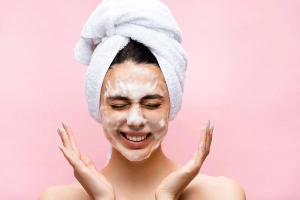 Sonriente hermosa mujer con toalla en el pelo y espuma en la cara aislada en rosa - foto de stock