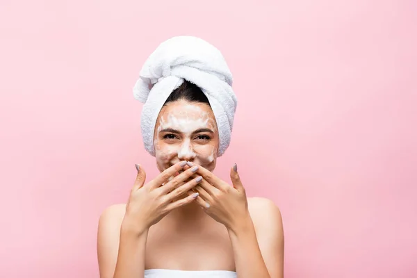 Riéndose hermosa mujer con toalla en el pelo y espuma en la cara aislada en rosa - foto de stock