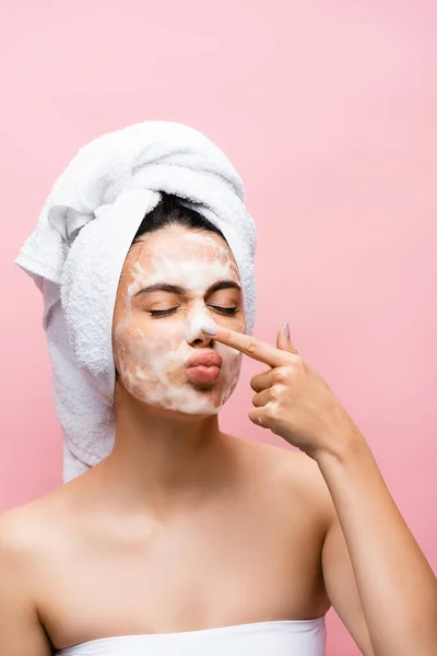 Belle femme avec serviette sur cheveux et mousse sur le visage toucher nez isolé sur rose — Photo de stock