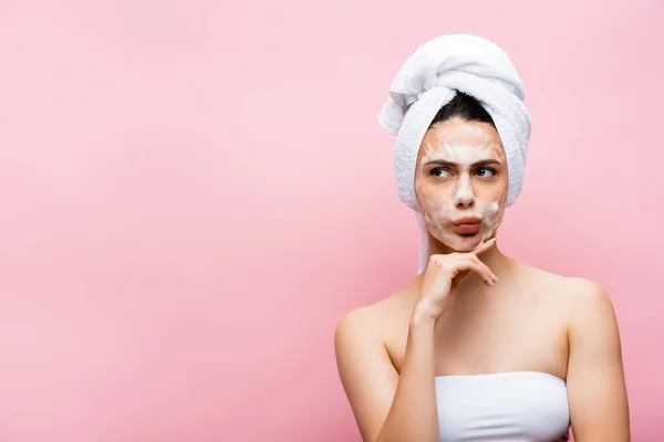 Pensive beautiful woman with towel on hair and foam on face isolated on pink — Stock Photo