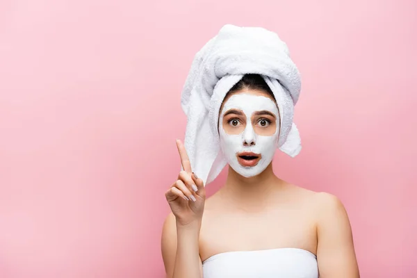 Choqué belle femme avec serviette sur la tête et masque d'argile sur le visage pointant de côté isolé sur rose — Photo de stock