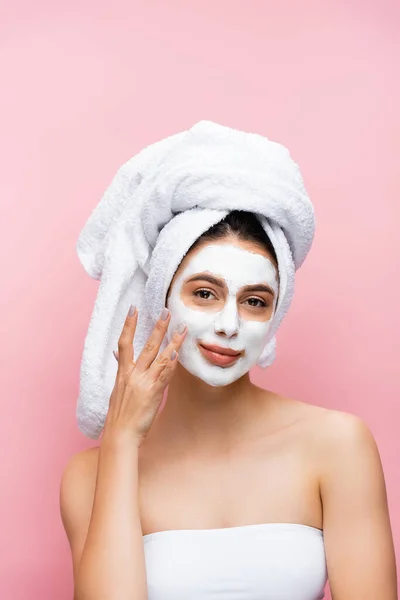 Smiling beautiful woman with towel on head and clay mask on face isolated on pink — Stock Photo