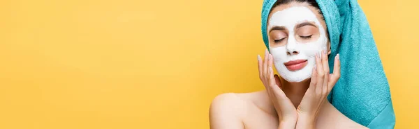 Beautiful woman with closed eyes, blue towel on hair and clay mask on face isolated on yellow, banner — Stock Photo