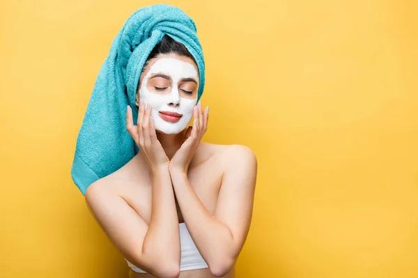 Beautiful woman with closed eyes, blue towel on hair and clay mask on face isolated on yellow — Stock Photo