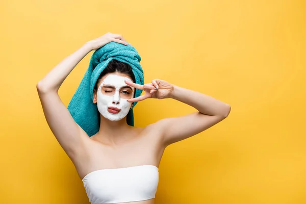 Hermosa mujer con toalla azul en el cabello y máscara de arcilla en la cara mueca aislado en amarillo - foto de stock