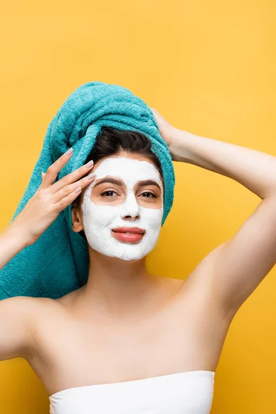 Beautiful woman with blue towel on hair and clay mask on face isolated on yellow — Stock Photo