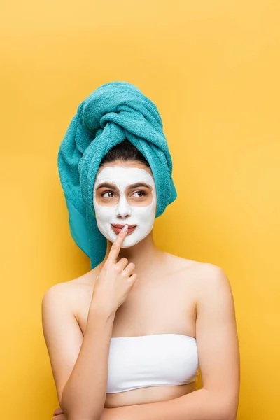 Mulher bonita pensativa com toalha azul no cabelo e máscara de barro no rosto isolado no amarelo — Fotografia de Stock