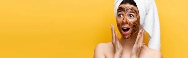 Choqué belle femme avec serviette sur la tête et masque de café sur le visage isolé sur jaune, bannière — Photo de stock