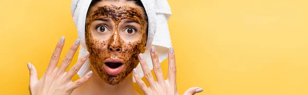 Shocked beautiful woman with towel on head and coffee mask on face isolated on yellow, banner — Stock Photo