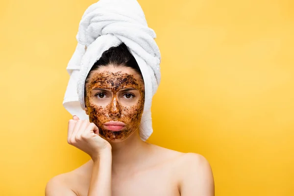 Sad beautiful woman with towel on head and coffee mask on face isolated on yellow — Stock Photo