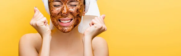 Bella donna con asciugamano sulla testa e maschera da caffè sul viso mostrando pugni isolati su giallo, banner — Foto stock