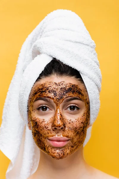 Beautiful woman with towel on head and coffee mask on face isolated on yellow — Stock Photo