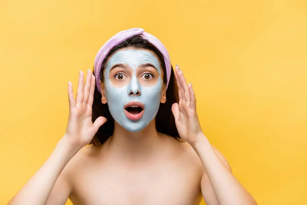Shocked beautiful woman with clay mask on face isolated on yellow — Stock Photo