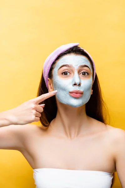 Hermosa mujer apuntando a la máscara de arcilla en la cara aislada en amarillo - foto de stock