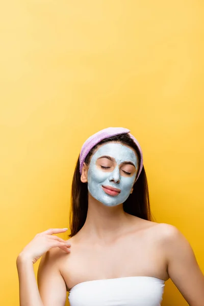 Bella donna con maschera di argilla sul viso e gli occhi chiusi isolati su giallo — Foto stock