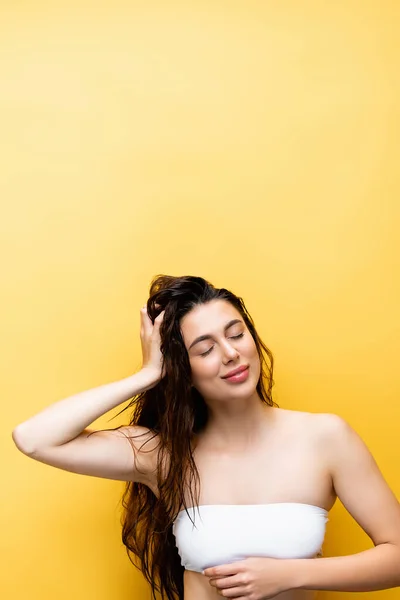 Sonriente hermosa mujer con el pelo mojado aislado en amarillo - foto de stock