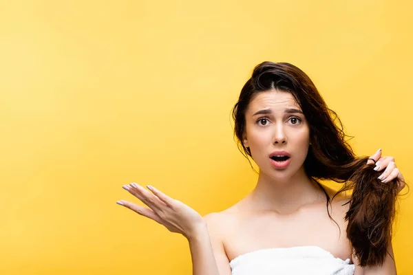 Shocked beautiful woman holding hair isolated on yellow — Stock Photo