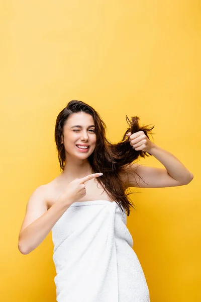 Bella donna sorridente che punta ai capelli isolati sul giallo — Foto stock