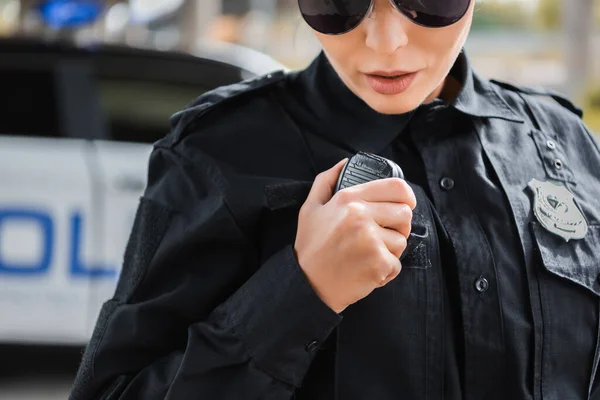 Vista ritagliata di giovane poliziotta che parla alla radio impostato su sfondo sfocato all'aperto — Foto stock