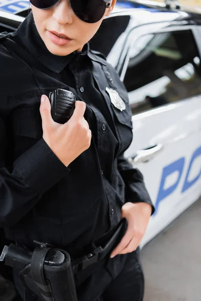 Обрезанный вид молодой женщины-полицейского, разговаривающей по радио на размытом фоне на открытом воздухе — стоковое фото